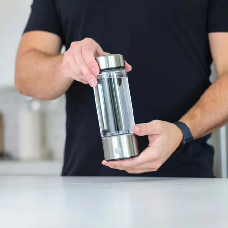 Person holding a glass hydrogen water bottle in a bright kitchen