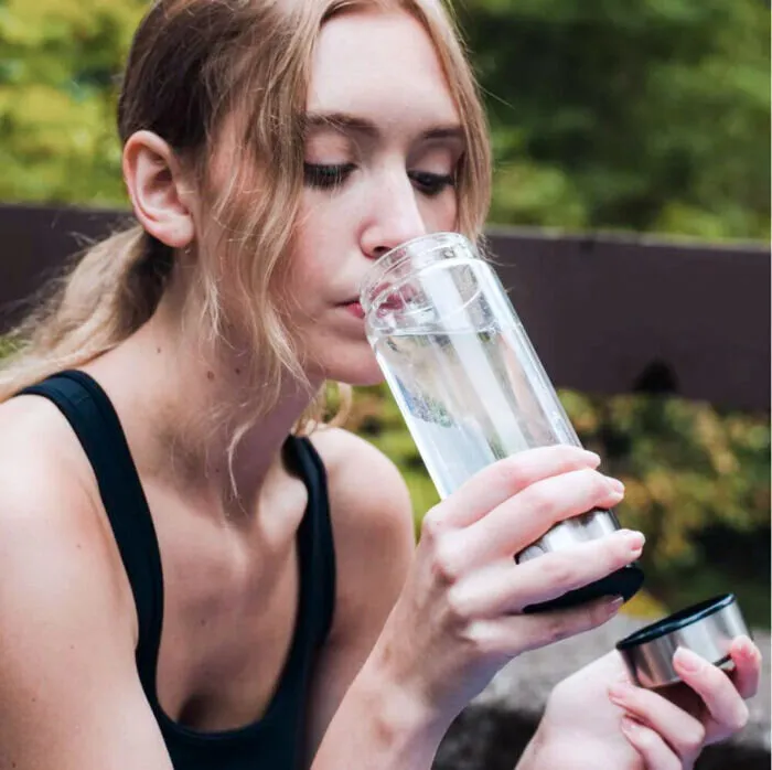 Woman outdoors sipping water from the glass bottle with the lid in her other hand